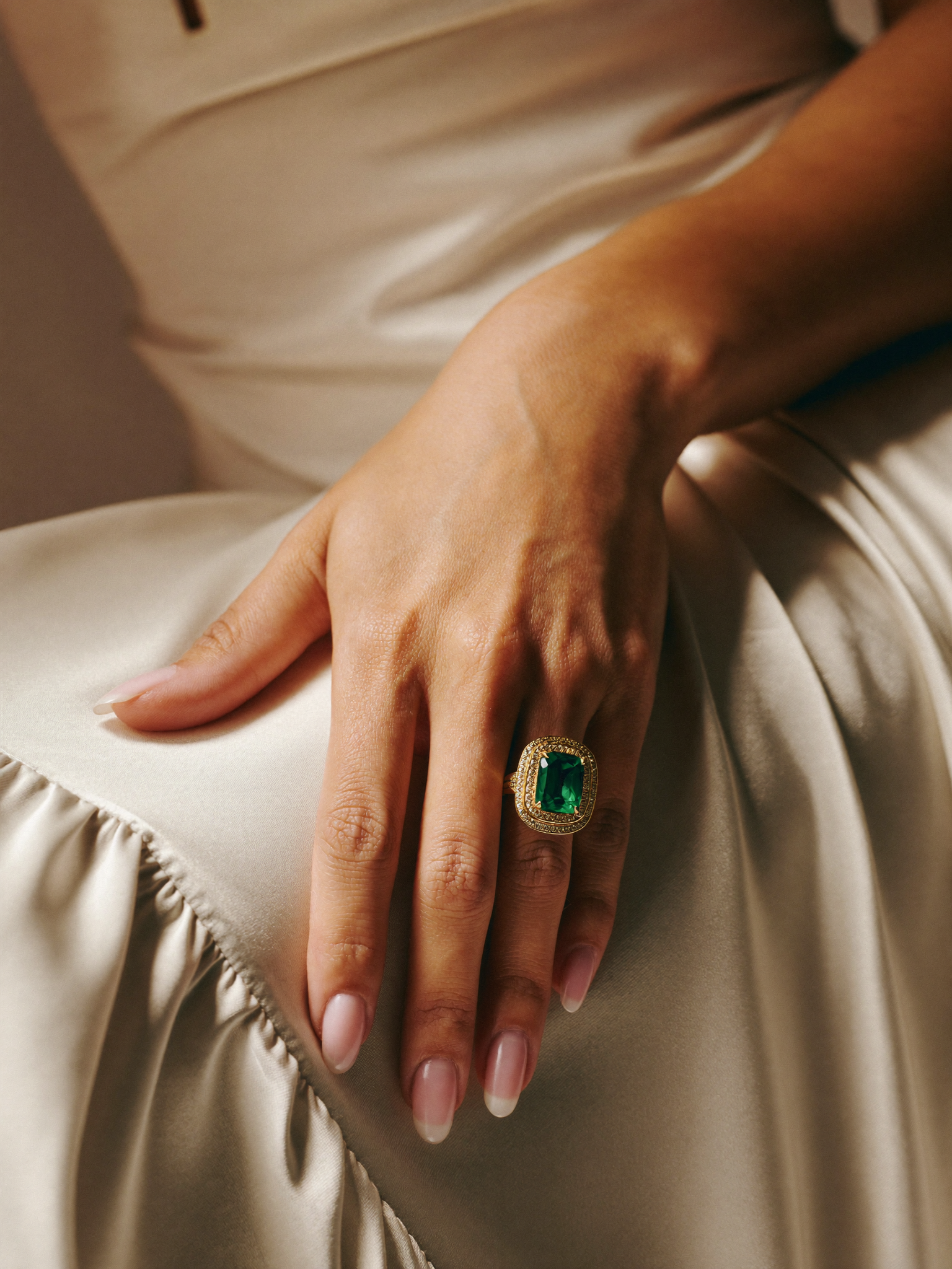 Anel de esmeralda cushion em ouro 18k JLópez · mão feminina sobre seda marfim