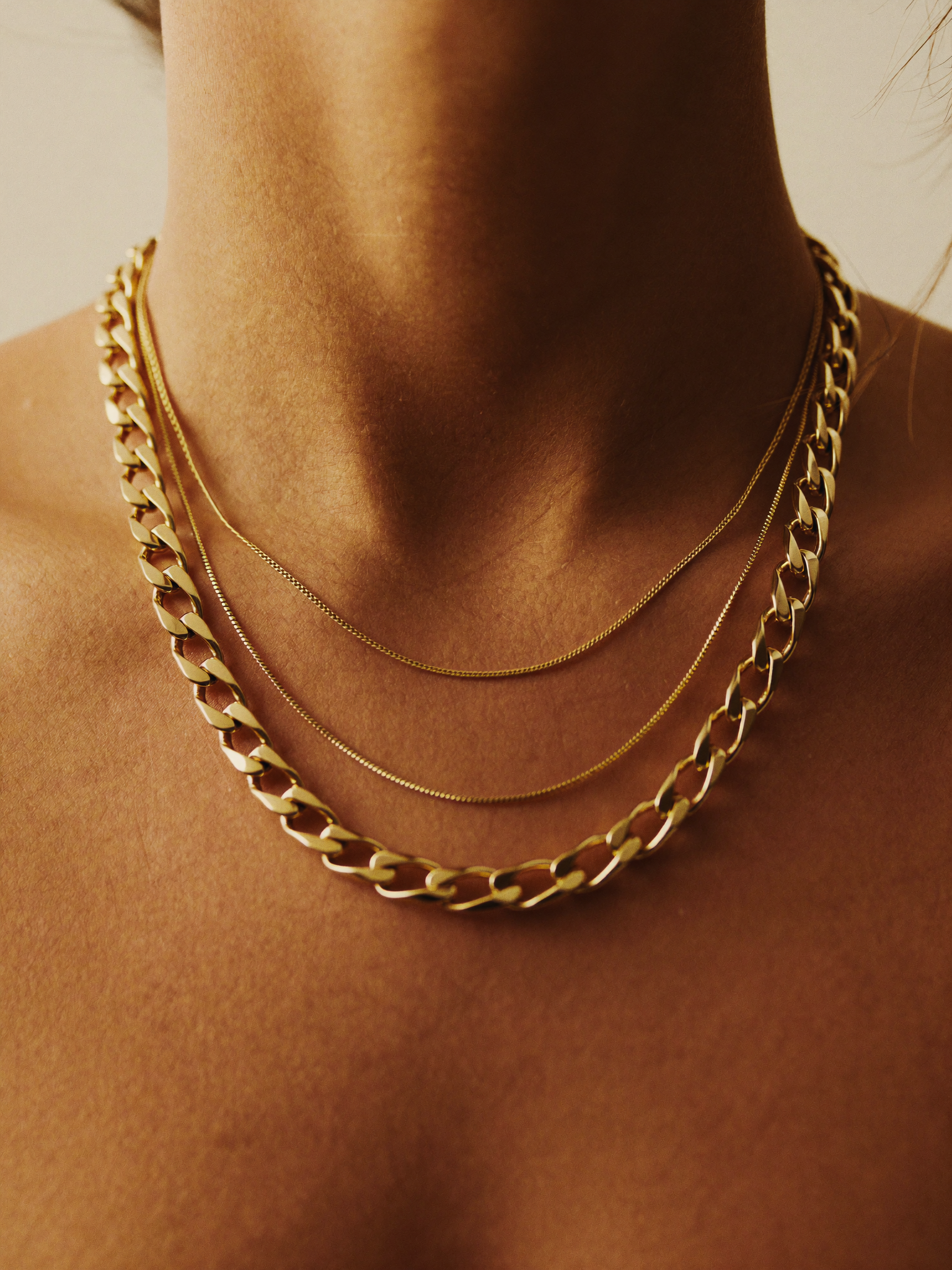 Três correntes de ouro 18k empilhadas sobre colo · layering editorial Tiffany