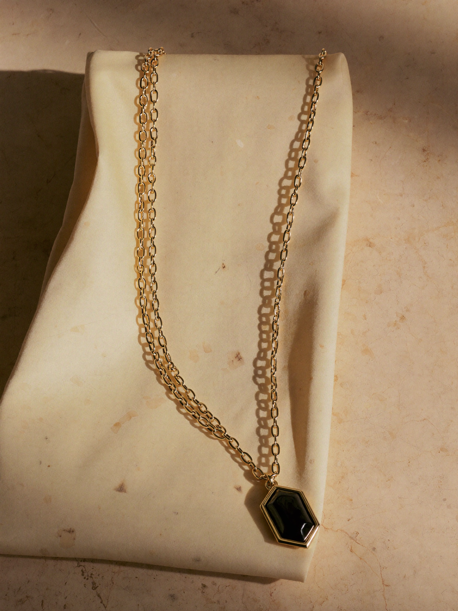 Colar com pingente obsidiana hexagonal em ouro 18k · still-life sobre travertino