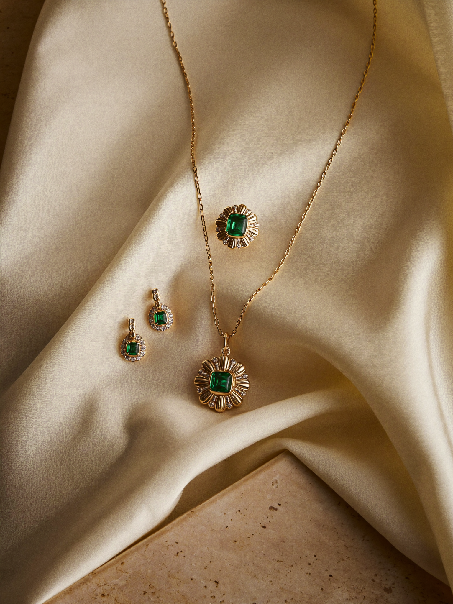 Conjunto de esmeraldas em flat-lay sobre seda marfim e travertino · ouro 18k JLópez